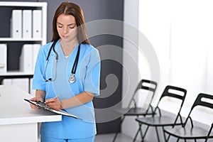 Doctor woman at work. Portrait of female physician filling up medical form while standing near reception desk at clinic