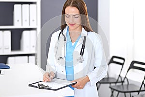 Doctor woman at work. Portrait of female physician filling up medical form while standing near reception desk at clinic