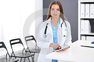 Doctor woman at work. Portrait of female physician using digital tablet while standing near reception desk at clinic or