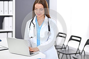 Doctor woman at work. Portrait of female physician using laptop computer while standing near reception desk at clinic or