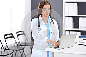 Doctor woman at work. Portrait of female physician using laptop computer while standing near reception desk at clinic or