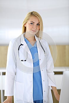 Doctor woman at work while standing straight in hospital or clinic. Blonde cheerful physician ready to help patients