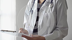 Doctor woman at work using a white clipboard while writing medical notes. An unknown physician standing near the