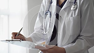 Doctor woman at work using a white clipboard while writing medical notes. An unknown physician standing near the