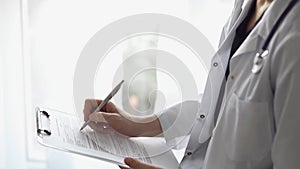 Doctor woman at work using a white clipboard while writing medical notes. An unknown physician standing near the