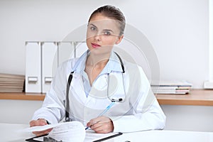 Doctor woman writing papers at the desk in hospital office. Medicine and over work concept