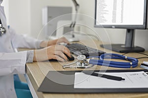 Doctor working at computer and typing electronic medical record sitting near stethoscope.