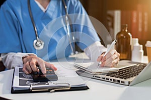 Doctor working on desk use calculator with laptop computer and paperwork in the office.