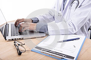 Doctor working on desktop computer and prescription paper