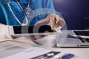 Doctor working on laptop computer and tablet and medical stethoscope on clipboard on desk