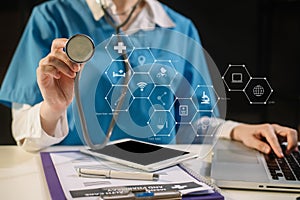 Doctor working on laptop computer and tablet and medical stethoscope on clipboard on desk.