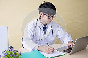 Doctor working with laptop computer and  writing on paperwork