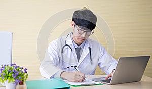 Doctor working with laptop  computer and writing on paperwork