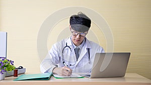 Doctor working with  laptop computer and writing on paperwork