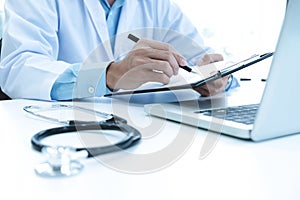 Doctor working with laptop computer and writing on paperwork