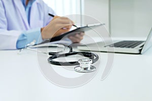 Doctor working with laptop computer and writing on paperwork. Ho