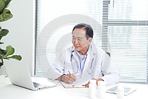 Doctor working with laptop computer and writing on paperwork in the hospital