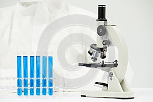 Doctor working with an optical microscope in a medical laboratory with test tubes on the table