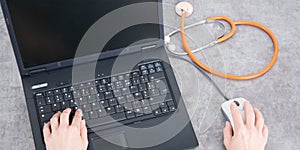 Doctor is working the prescriptions on his laptop with a stethoscope resting on his desk photo