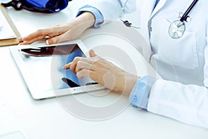 Doctor working table. Woman physician using tablet computer while sitting in hospital office close-up. Healthcare
