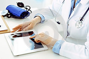 Doctor working table. Woman physician using tablet computer while sitting in hospital office close-up. Healthcare