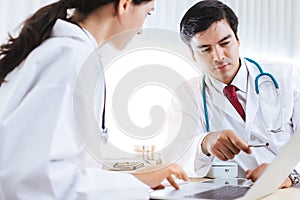 Doctor working with team on laptop computer in doctorÃ¢â¬â¢s office or hospital room. Senior doctor advice, teaching junior doctor photo