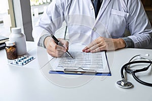 Doctor working and writing on paper report in hospital and medical stethoscope, medicine on clipboard on desk