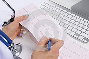 Doctor workplace. Electrocardiogram, ecg in hand of a female doctor with ekg graph paper in hospital office room with computer