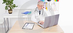 Doctor works at a laptop at his desk in clinic