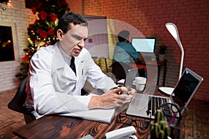 The doctor works on New Year`s Eve. He looks at something on the tablet.
