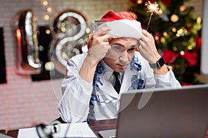 The doctor works on New Year`s Eve. He sits with a bored face. Against the backdrop of a Christmas tree.