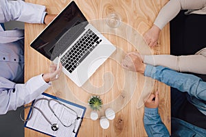 Doctor writing down medical records and talking with a couple during a visit, desktop top view, unrecognizable people