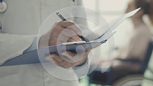 Doctor writing medical records and patient in a wheelchair