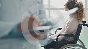 Doctor writing medical records and patient in a wheelchair