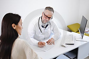 Doctor writing on a prescription note in medical office. Woman at the doctor`s appointment.
