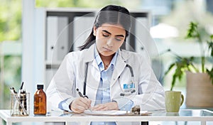 Doctor writing a prescription or recommending medication letter while sitting at her desk. Professional female GP