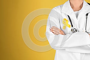 Doctor with yellow ribbon on robe against color background. Cancer awareness concept
