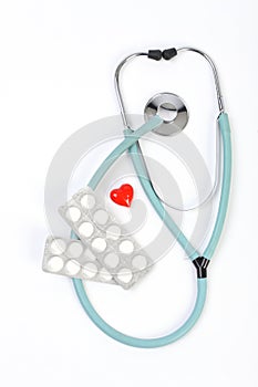 Doctors blue stethoscope, pills and one small red heart on white background