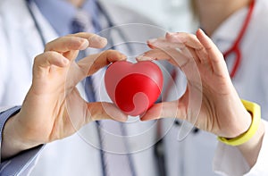 Doctors cardiologists hold red toy heart in clinic closeup