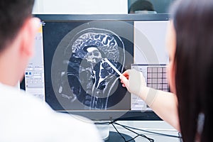 Doctors consider and discuss magnetic resonance image MRI of the brain. Back view, selective focus