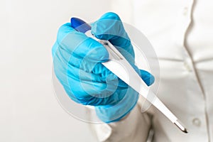 A doctors hand in a blue glove holds a electronic thermometer close up on a light background. High temperature, symptoms of a