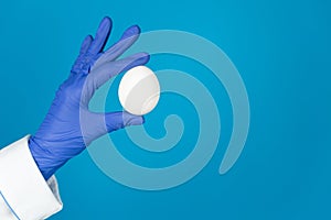 Doctors hand in a glove holds an egg on a blue background with copy space