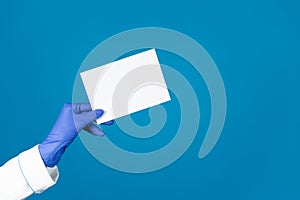 Doctors hand in a glove holds an envelope on a blue background with copy space