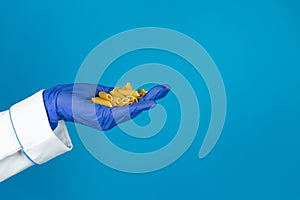 Doctors hand in a glove holds a macaroni pasta on a blue background with copy space