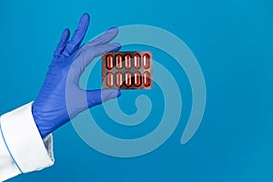 Doctors hand in a glove holds a paracetamol pills on a blue background with copy space