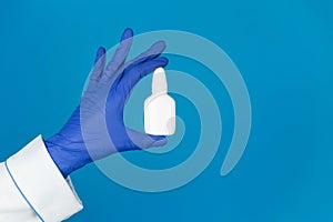 Doctors hand in a glove holds a white nasal spray for runny nose on a blue background with copy space