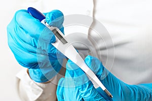 The doctors hands in blue gloves hold a electronic thermometer on a light background, checking the patients high temperature,