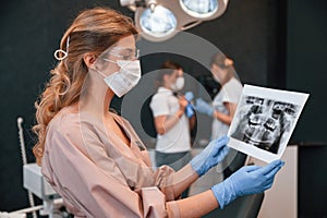 Doctors are indoors. Woman holding and looking at x-ray. In the stomatological cabinet