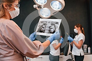 Doctors are indoors. Woman holding and looking at x-ray. In the stomatological cabinet