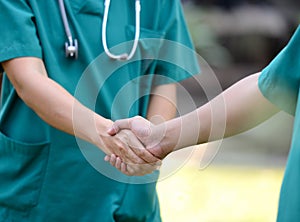 Doctors in a medical team handshake together outdoor on the green park background (volunteer)